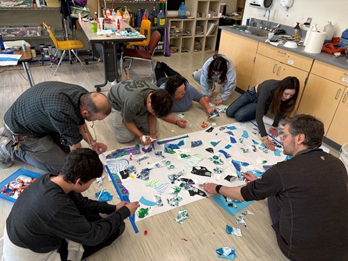 Seven students and teachers create a large ice art collage on the floor
