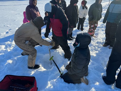 Two students use a hand auger to drill a hole in lake ice